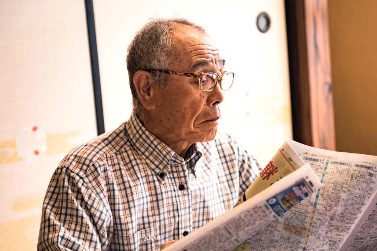 雨上がりの濡れた路面と曇り空を見上げて自転車を押して歩くシニア男性