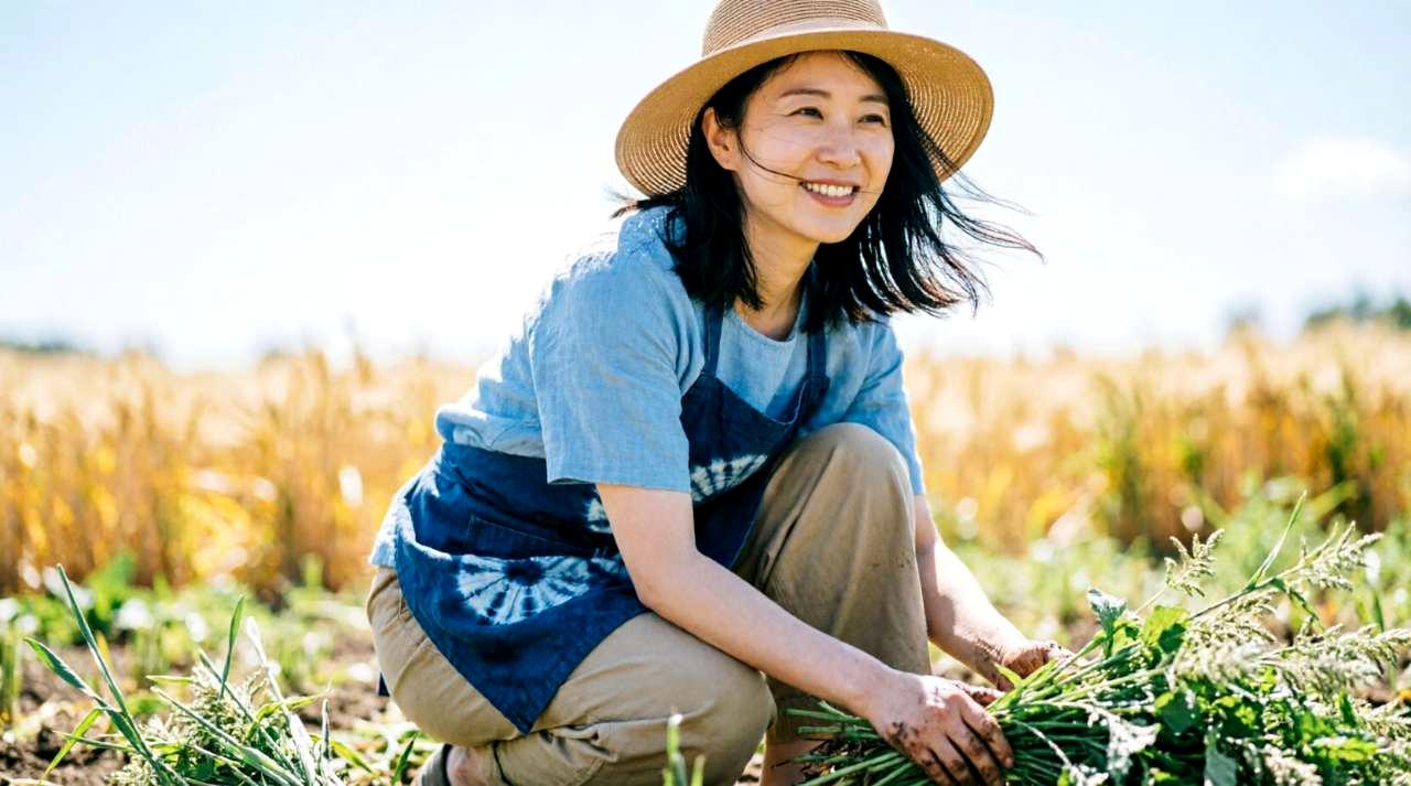 50代の男性が緑豊かな家庭菜園で野菜を収穫し、穏やかに微笑んでいる様子